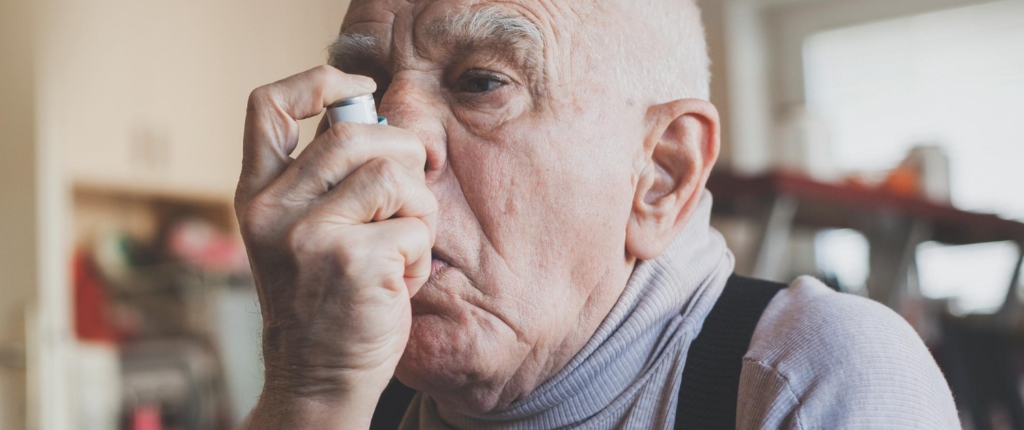 Ein älterer Mann inhaliert mithilfe eines Inhalators