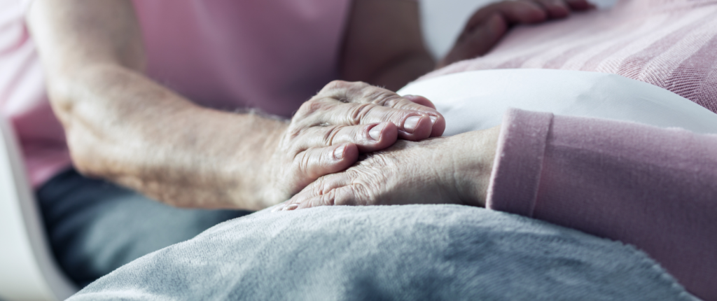 Sterbehilfe: Ein Mann hält einer alten Frau, die in einem Bett liegt, die Hand.