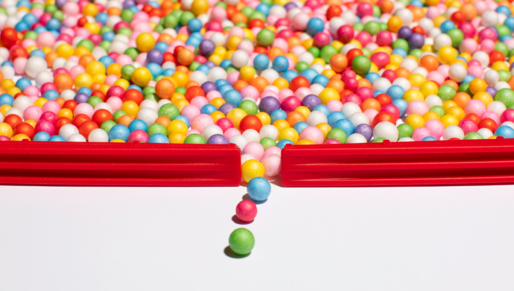 Viele kleine bunte Kugeln, die sich durch eine kleine Öffnung drängen.