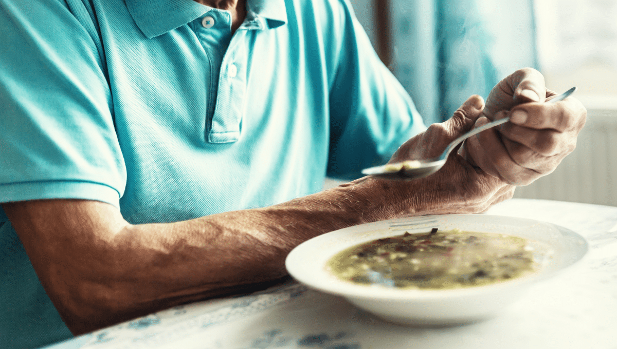Ein Mann stützt seine Hand, um mit einem Löffel Suppe essen zu können.