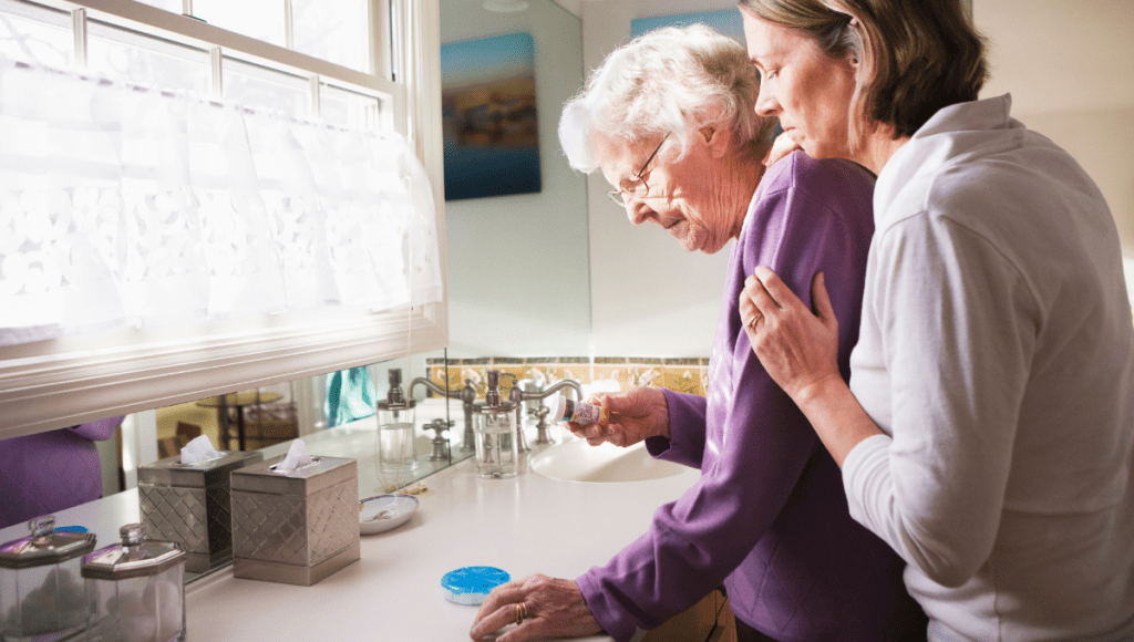 Eine Tochter umarmt ihre pflegebedürftige Mutter, die eine Dose mit Tabletten in der Hand hält.