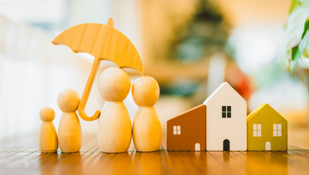 Eine Familie aus Holz-Spielfiguren steht unter einem Regenschirm.
