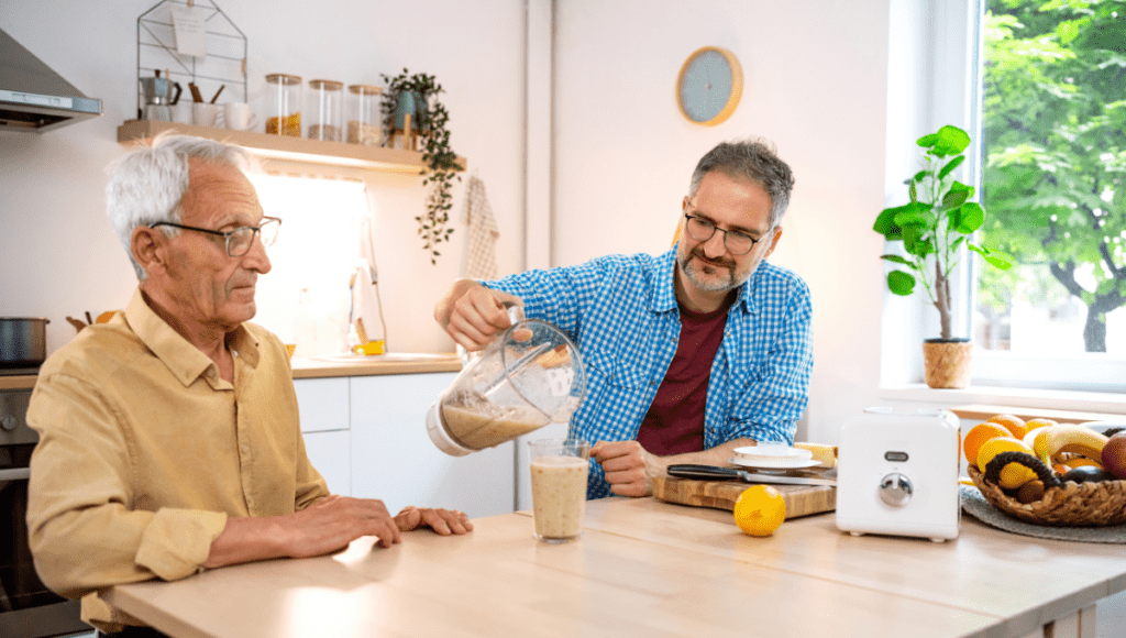 Ein Senior mit Mangelernährung bereitet zusammen mit seinem Sohn einen gesunden Smoothie vor als eine der wichtigsten Maßnahmen.