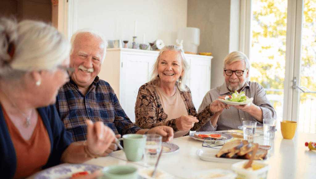 Wohnen im Alter: Mehrere Senioren, sitzen gemeinsam an einem großen Tisch und unterhalten sich beim Essen.