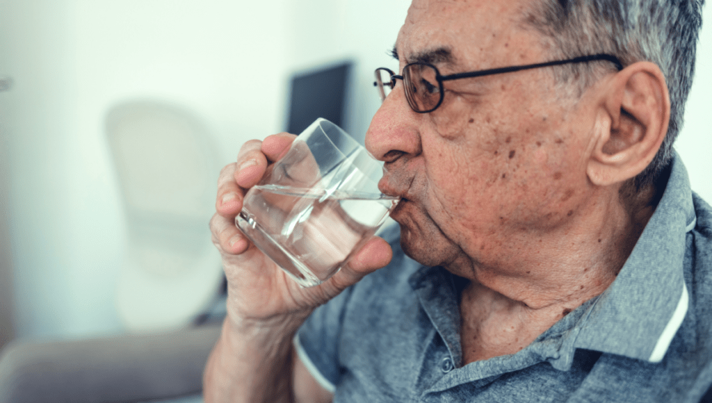 Ein älterer Mann trinkt ein Glas Wasser, damit sein trockener Mund besser wird.