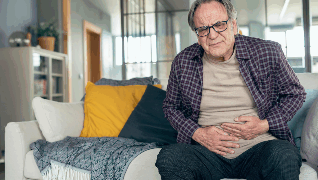 Ein Mann sitzt mit Magen-Darm auf dem Sofa und hält sich den Bauch.