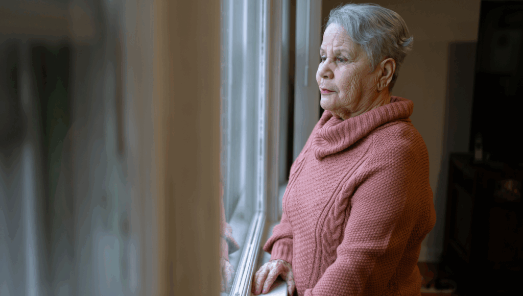 Eine Frau mit Pflegebedürftigkeit hat Angst, das Haus zu verlassen und schaut aus dem Fenster ihrer Wohnung.