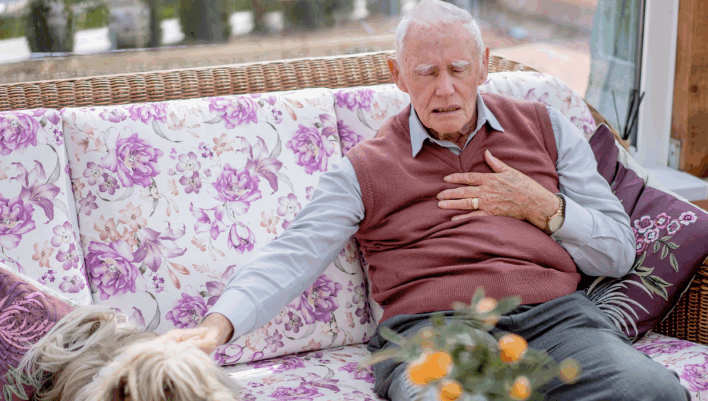 Ein pflegebedürftiger Mann sitzt auf dem Sofa und hält sich die Brust, weil er Atemprobleme hat.